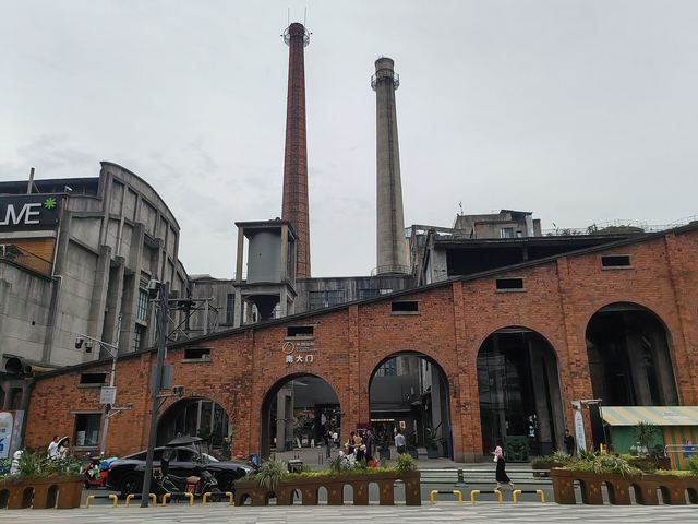 Red-brick factory halls with arched openings and two tall chimneys above the south gate