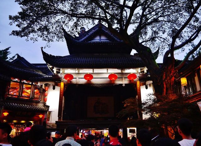 Red lanterns on a traditional stage front at Jinli Street, watched by a night crowd